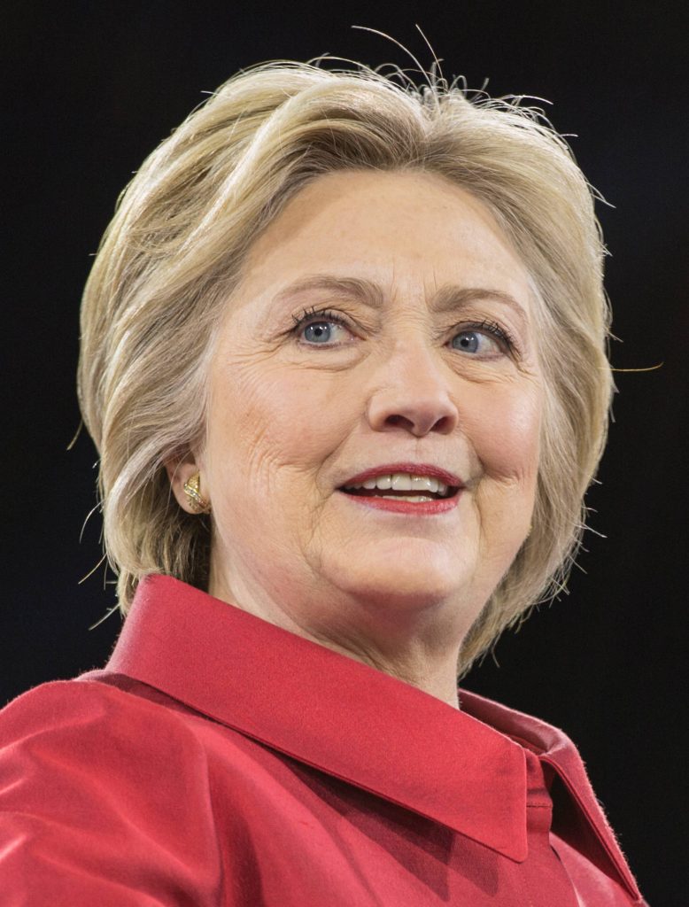 Portrait of Hillary Clinton in vibrant red jacket with warm smile and dark background wallpaper