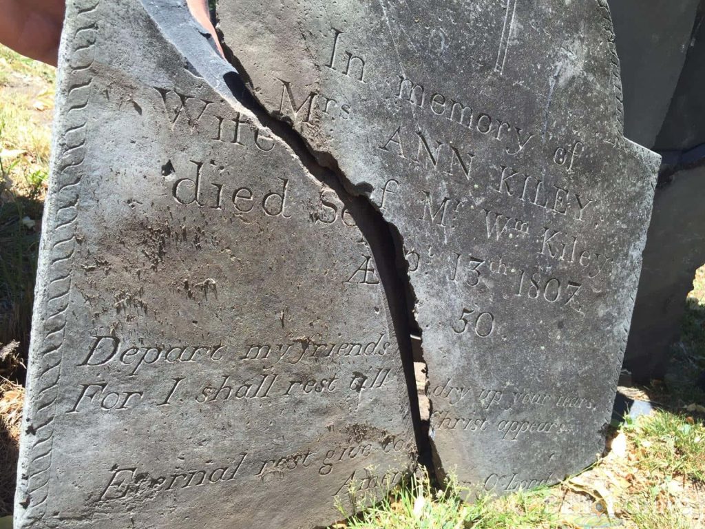 Weathered 1807 gravestone of Ann Kiley with vertical crack in sunlit historic cemetery Wallpaper