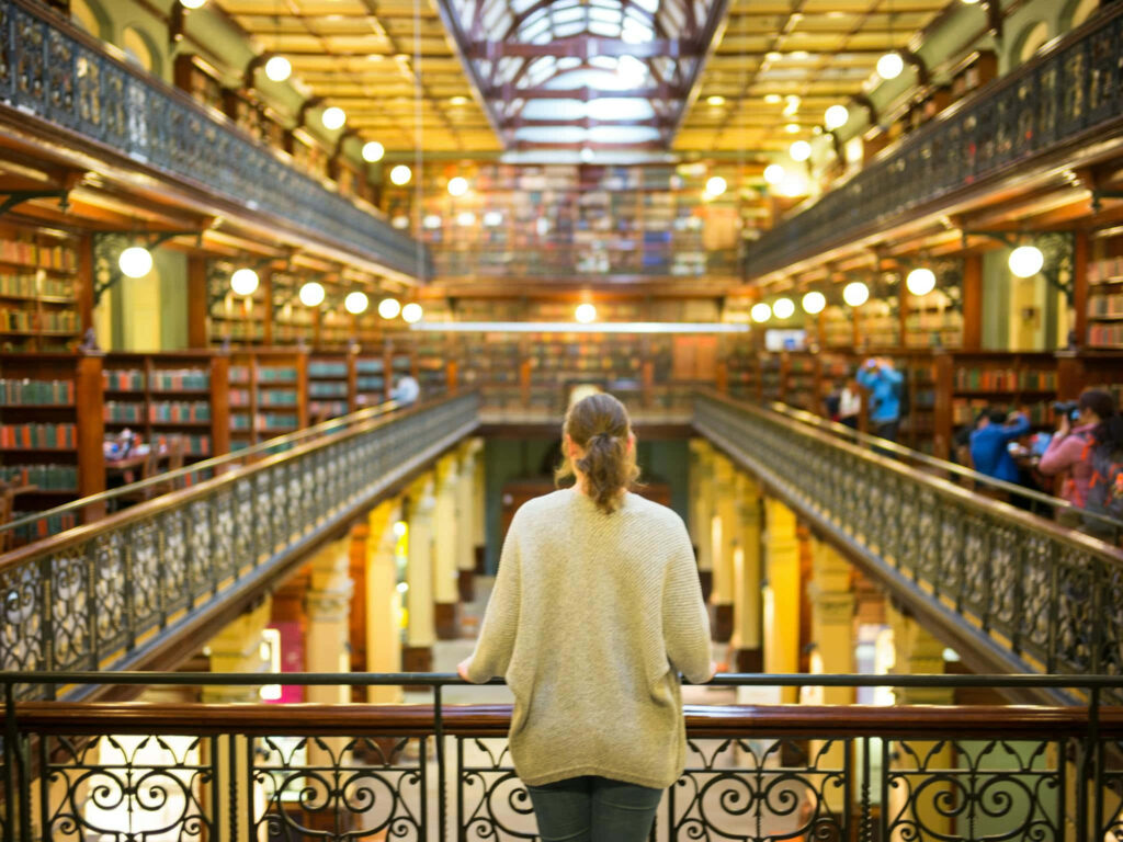 Visitor exploring grand historic Adelaide State Library interior with elegant iron railings and books Wallpaper