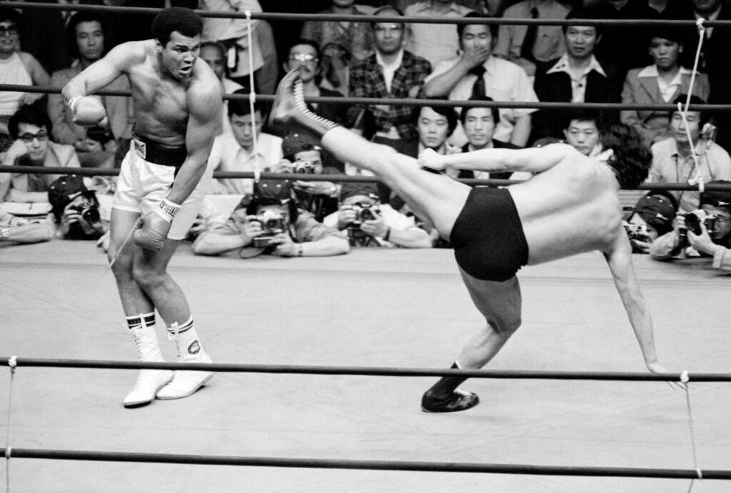 Historic black and white image of Antonio Inoki leg kick fighting Muhammad Ali in boxing ring Wallpaper