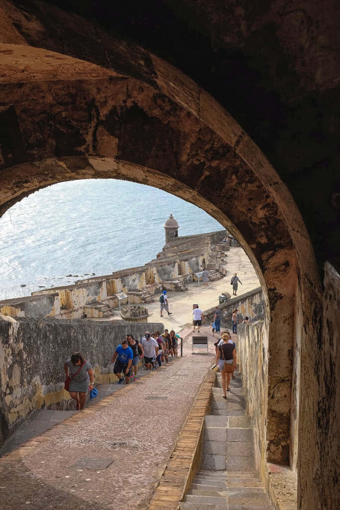 Tourists walking historic stone path at Castillo San Felipe del Morro with ocean views wallpaper