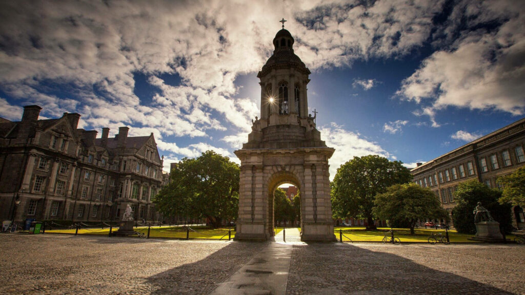 Majestic stone archway at historic Dublin university framed by trees under cloudy sky wallpaper