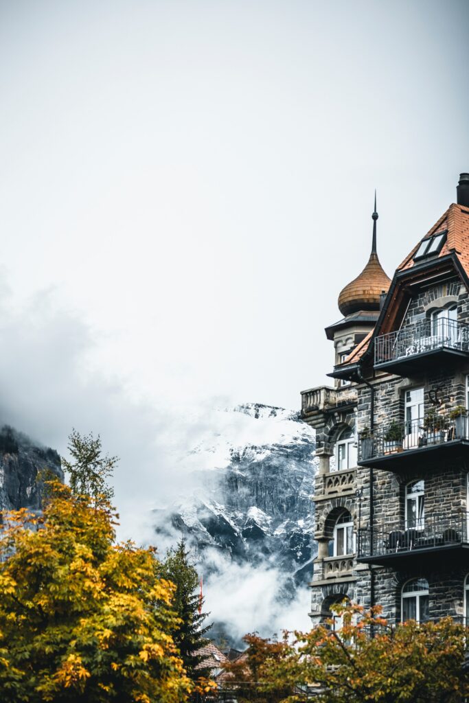 Historic European building with turret framed by autumn trees and misty snow-covered mountains wallpaper