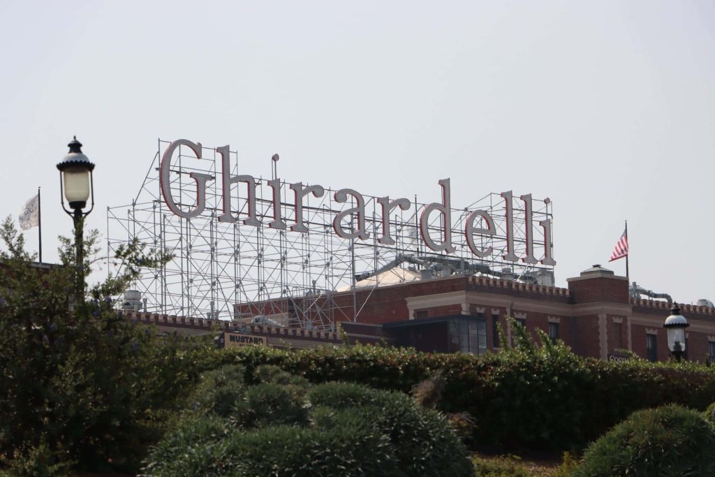 Historic Ghirardelli Square sign in San Francisco with red letters brick building and flag background Wallpaper