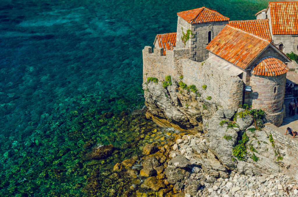 Mediterranean stone buildings with red roofs on cliffs overlooking turquoise sea bright wallpaper