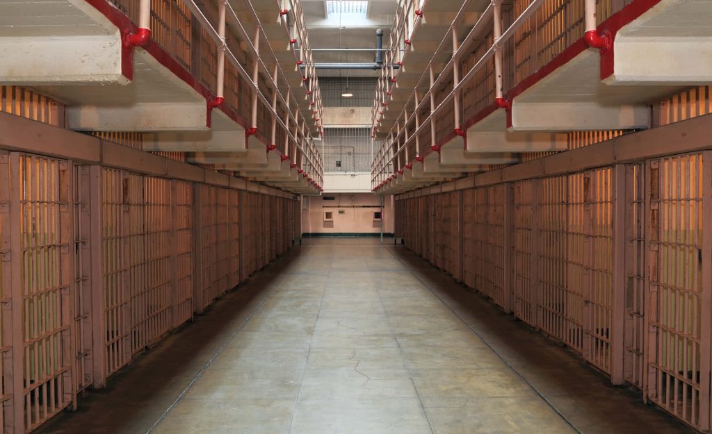 Historic prison cell block corridor with barred cells and red pipes vintage jail wallpaper