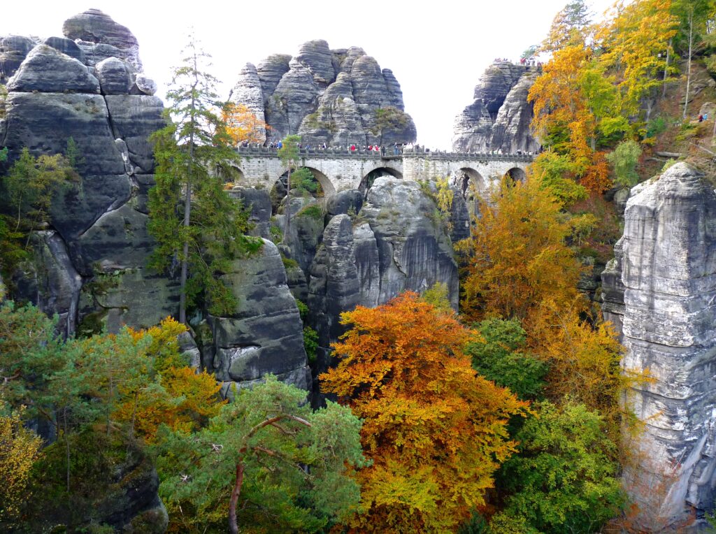 Historic stone bridge over river surrounded by vibrant autumn trees and dramatic rock formations Wallpaper