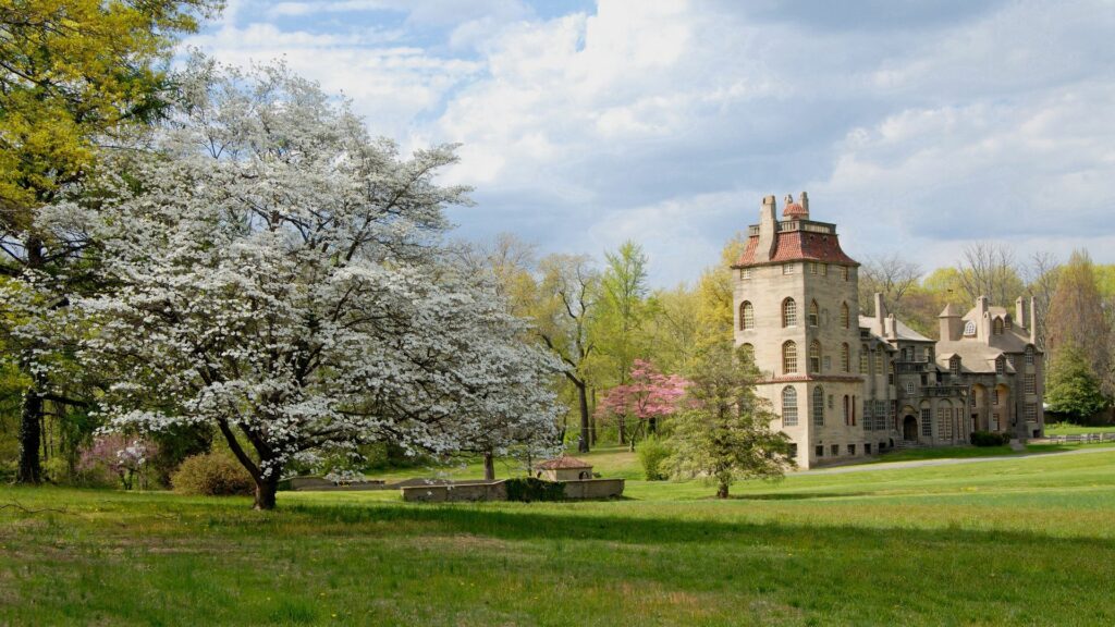 Historic stone building with lush green grass blooming flowers and vibrant trees in springtime Wallpaper