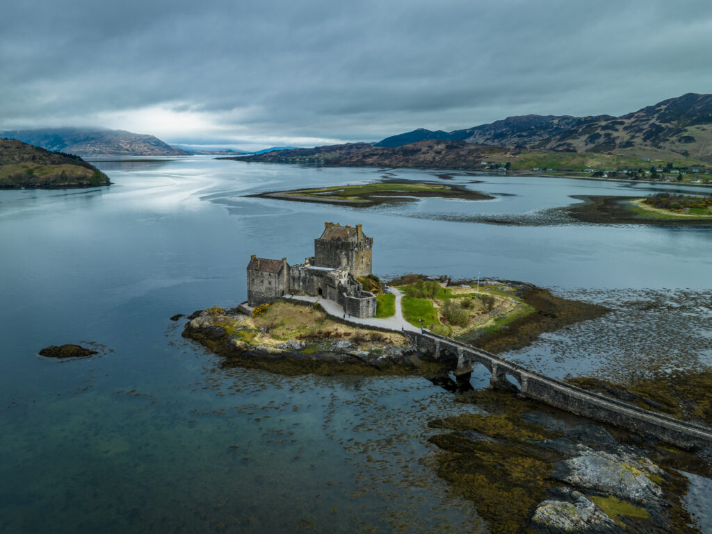 Historic stone building on island surrounded by lake and mountains under moody sky wallpaper
