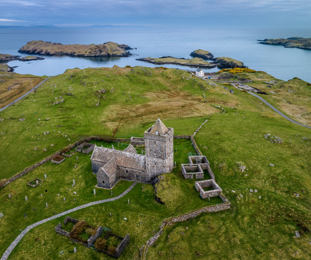 Aerial view of historic stone house and green shore by calm sea with distant islands and blue sky Wallpaper