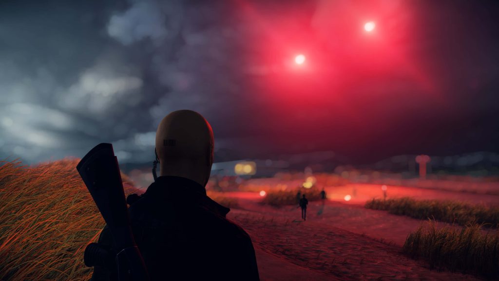 Hitman Agent 47 with rifle on grassy dune under glowing red sky cinematic stealth wallpaper