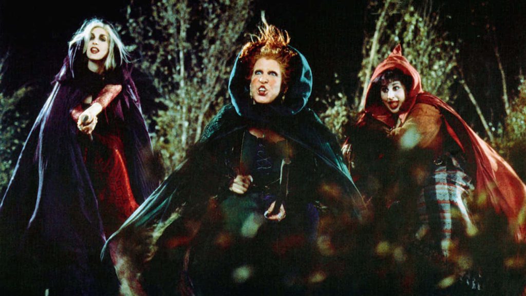 Hocus Pocus Sanderson Sisters in cloaks against dark forest Halloween spooky wallpaper background