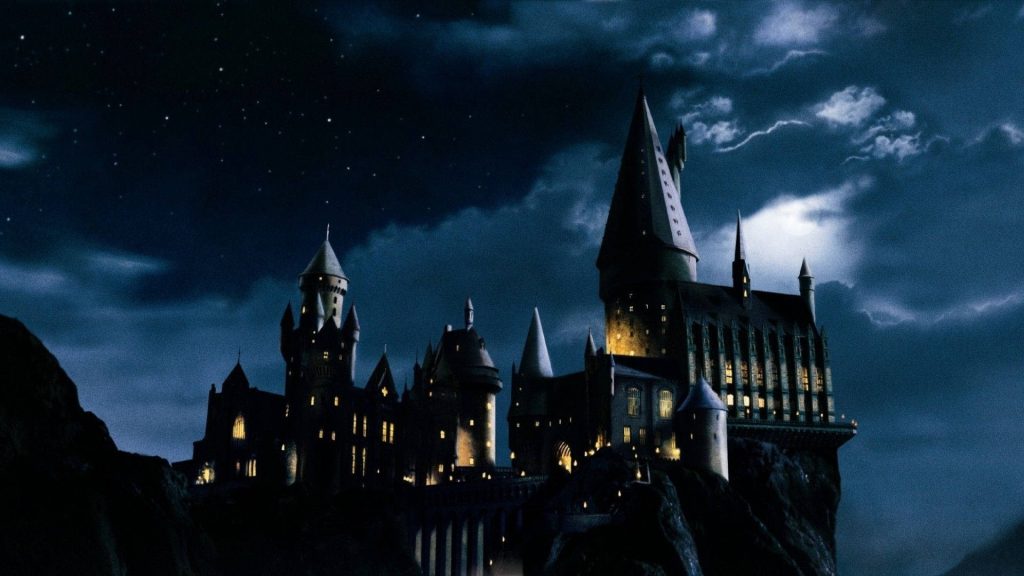 Hogwarts Castle at night with glowing windows against cliffs magical Harry Potter wallpaper