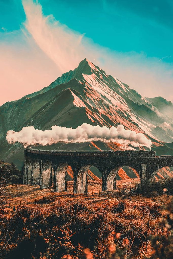 Hogwarts Express steam train crossing stone viaduct at sunset with mountains and turquoise sky Wallpaper