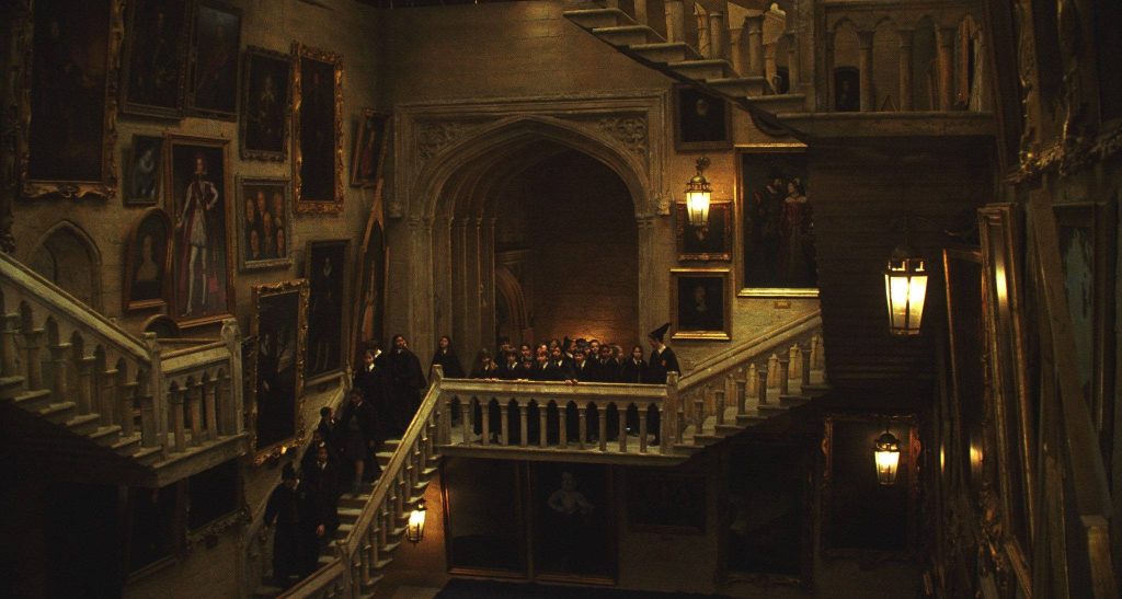 Hogwarts Grand Staircase wallpaper with students in robes stone walls portraits warm lantern light