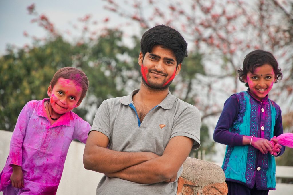Young man and two children joyfully celebrating Holi with pink gulal outdoors festive colors Wallpaper