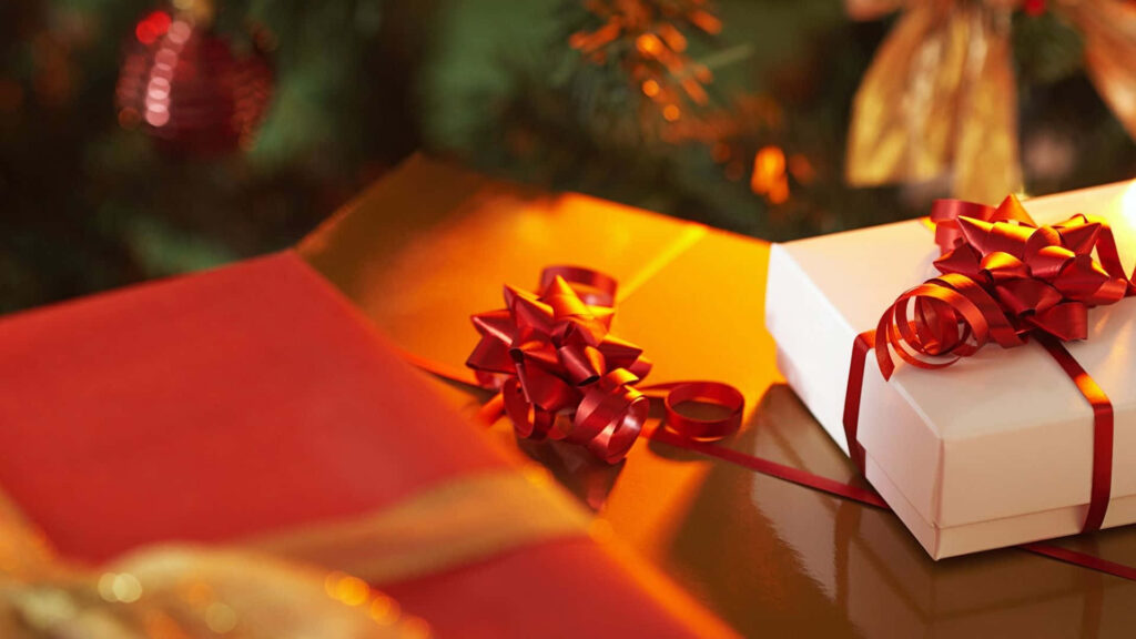 Holiday gifts wrapped with shiny red ribbons under decorated Christmas tree festive background Wallpaper
