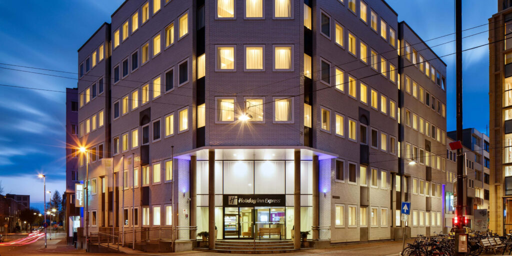 Holiday Inn Express Arnhem exterior warmly lit at twilight with glowing windows and calm sky Wallpaper