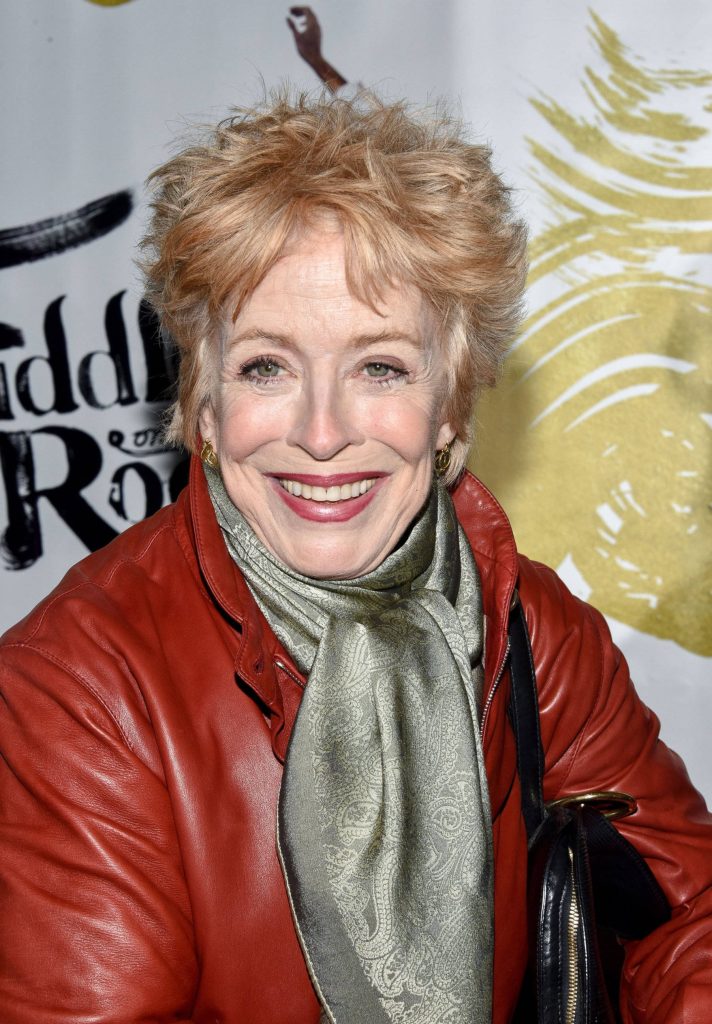 Holland Taylor in red leather jacket and olive scarf smiling at professional event backdrop wallpaper