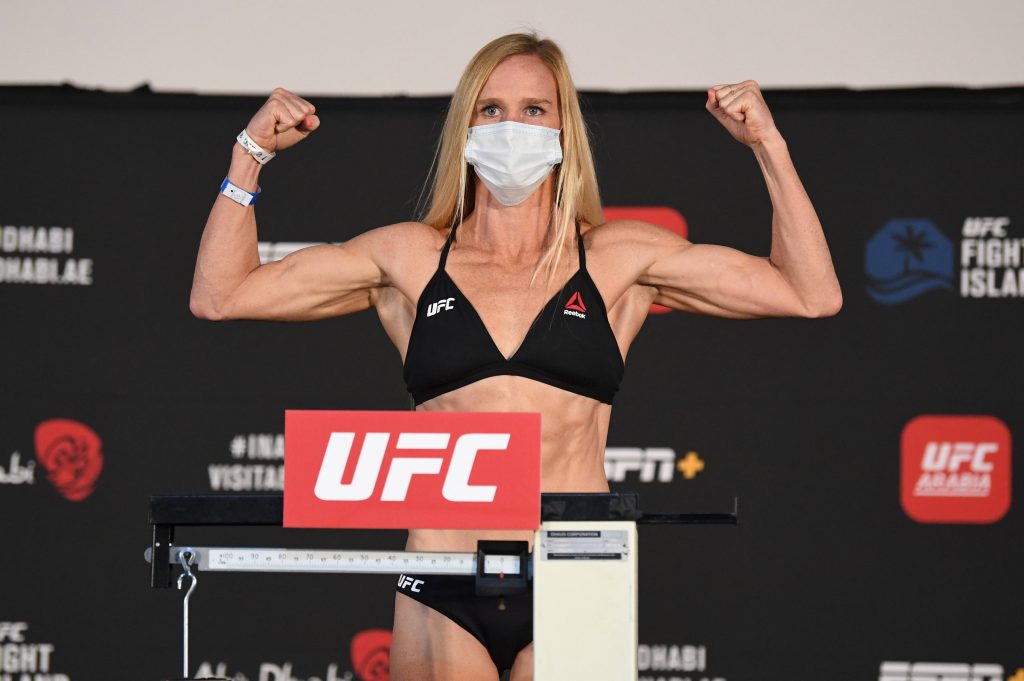 UFC fighter Holly Holm flexes biceps at official weigh-in in black Reebok sports bra and mask Wallpaper