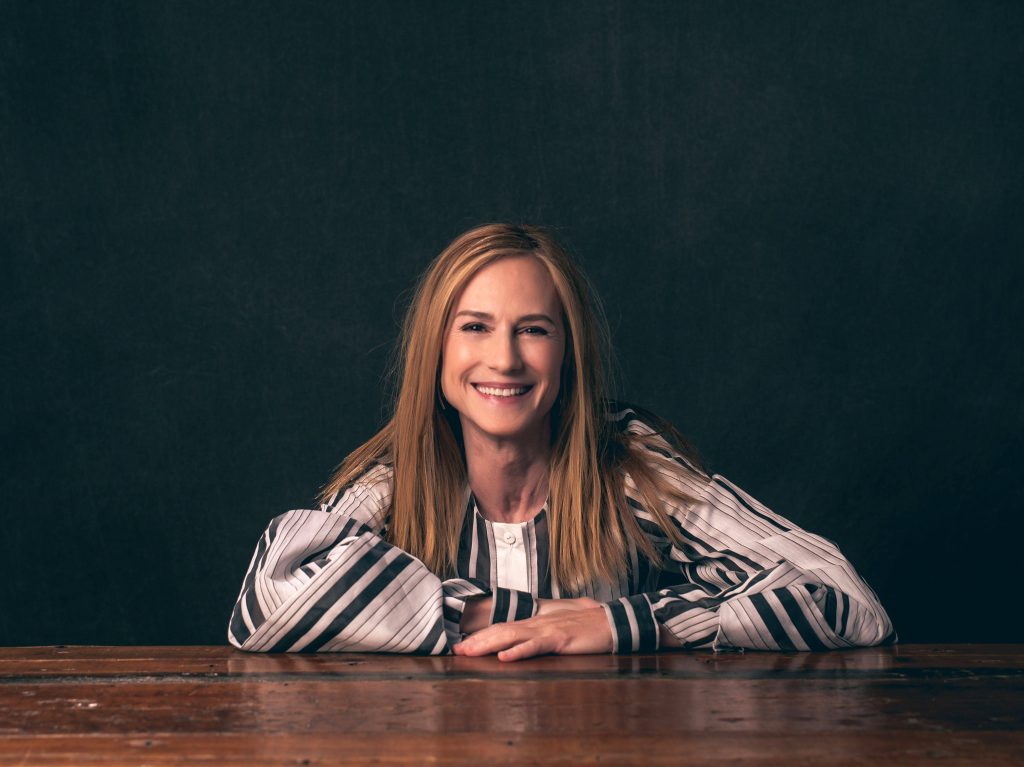 Holly Hunter smiling in black and white striped top sitting at wooden table studio portrait Wallpaper
