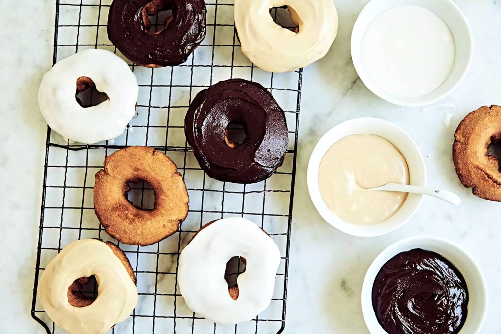 Assorted chocolate and white glazed donuts cooling on wire rack with fresh icing bowls on marble Wallpaper