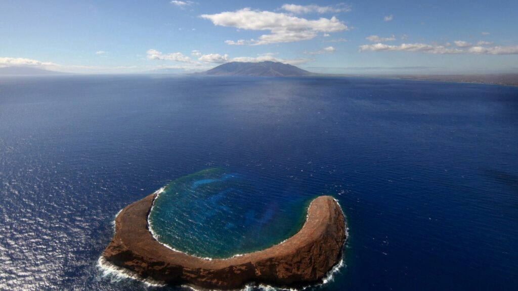 Aerial view of horseshoe island arch surrounded by deep blue ocean and scattered clouds wallpaper
