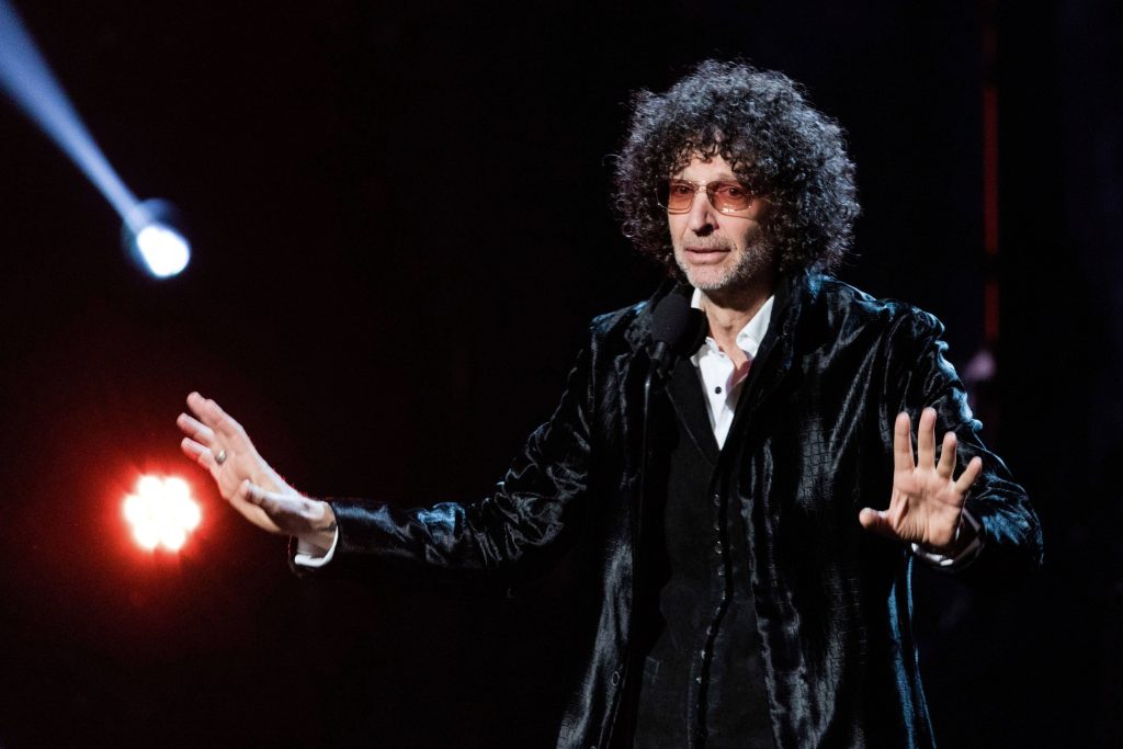 Howard Stern performing on stage with curly hair and tinted glasses dramatic lighting wallpaper
