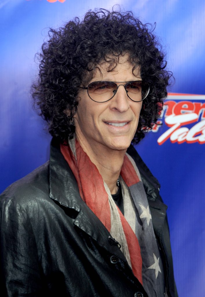 Howard Stern portrait with curly hair tinted glasses black jacket and American flag scarf blue background Wallpaper