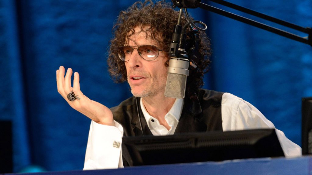 Howard Stern broadcasting in studio wearing tinted glasses and vest with blue background Wallpaper