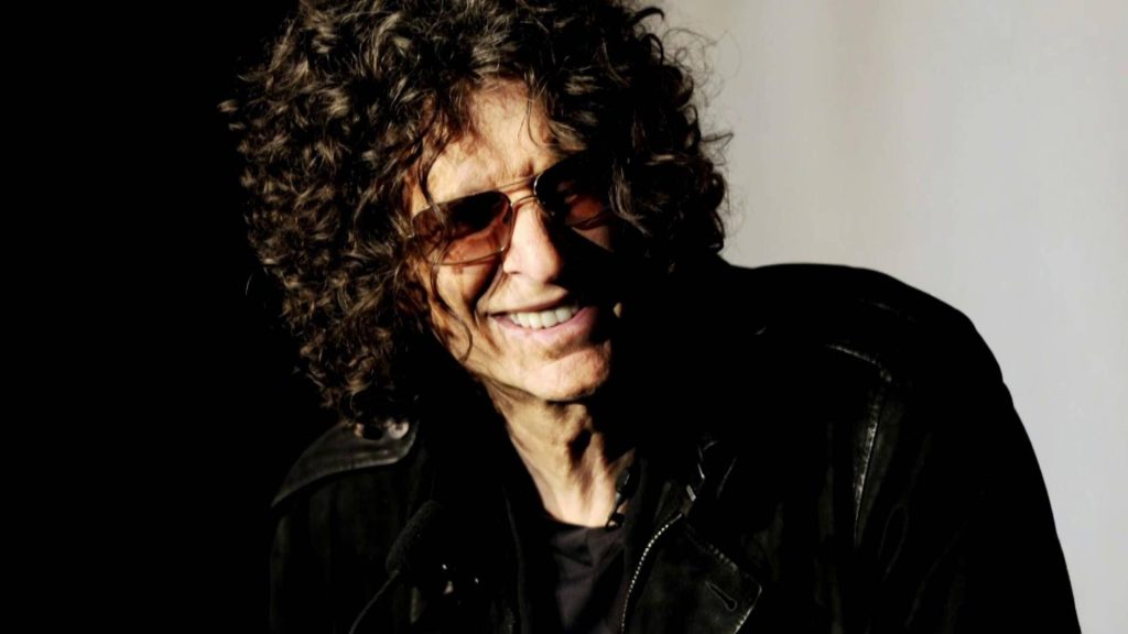 Howard Stern portrait wallpaper with curly hair tinted sunglasses warm smile dark background