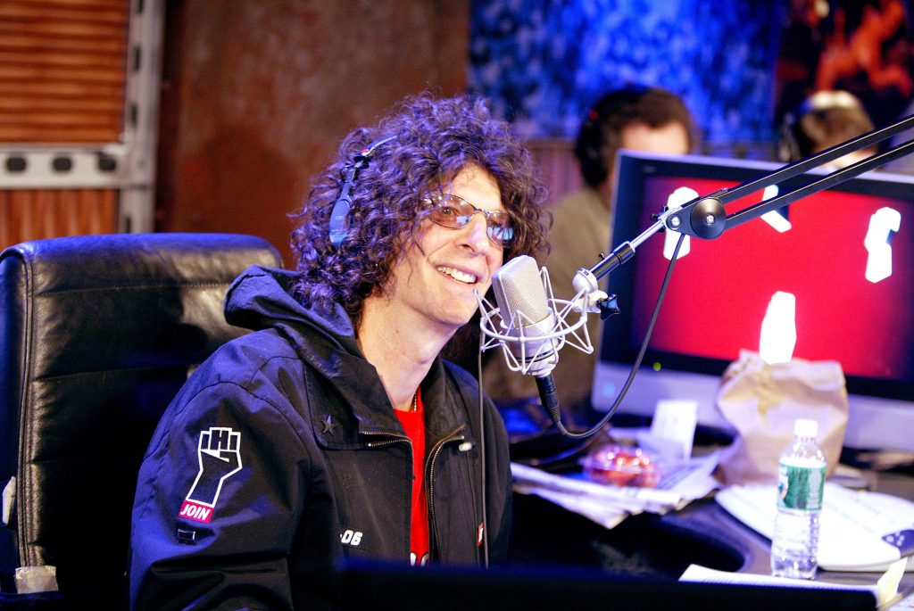 Howard Stern smiling in studio with curly hair, tinted glasses, and black jacket on mic Wallpaper