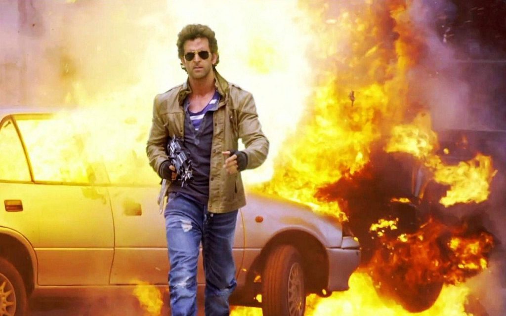 Hrithik Roshan walking from fiery car explosion wearing sunglasses rugged jacket holding weapon wallpaper
