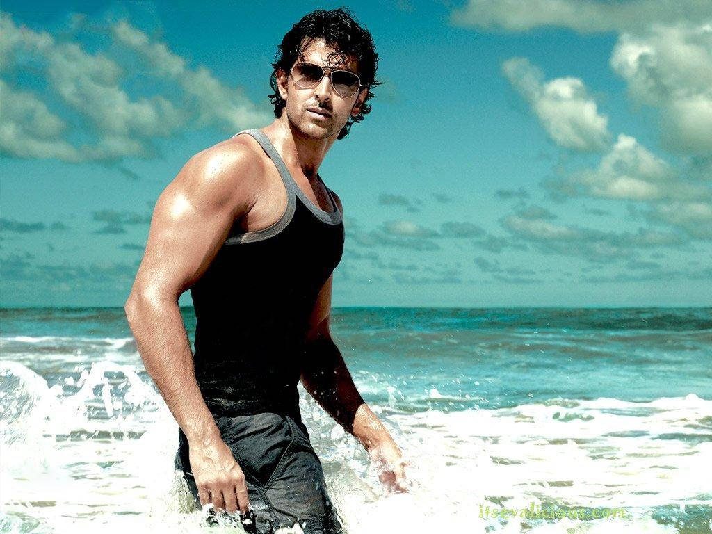 Bollywood star Hrithik Roshan in black tank top and sunglasses wading ocean waves sunny beach Wallpaper