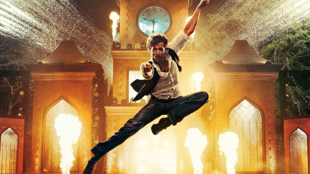 Hrithik Roshan mid-air dance pose with clock tower and fiery Bollywood background wallpaper