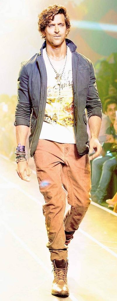 Hrithik Roshan walking fashion runway white graphic tee dark jacket casual trousers bright stage lighting Wallpaper