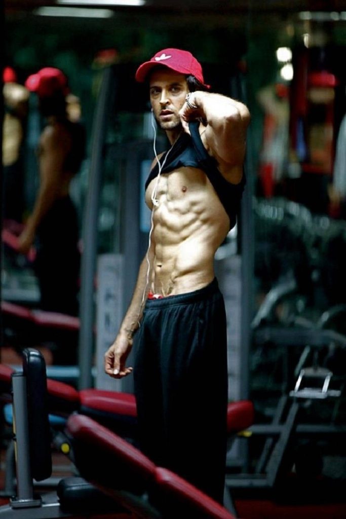 Hrithik Roshan showing ripped abs in gym wearing red cap and earphones intense workout wallpaper