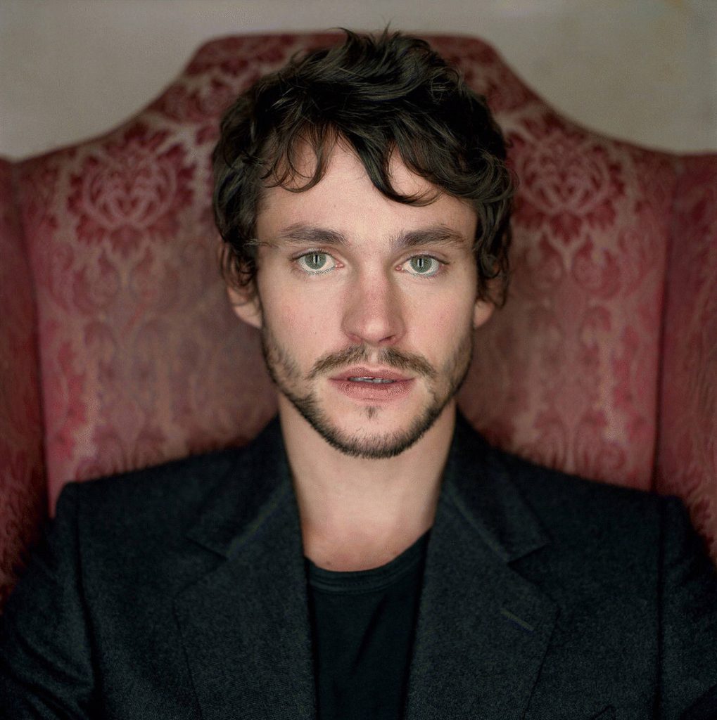 Portrait of actor Hugh Dancy with green eyes and blazer on vintage red tufted chair background Wallpaper