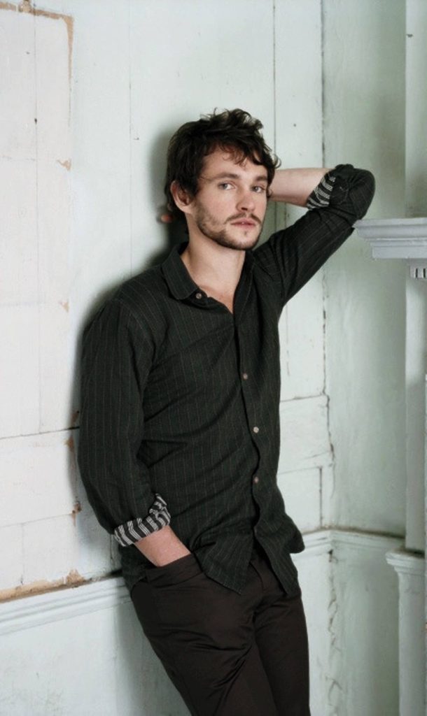 Hugh Dancy portrait in dark shirt with striped cuffs against rustic white wall wallpaper background