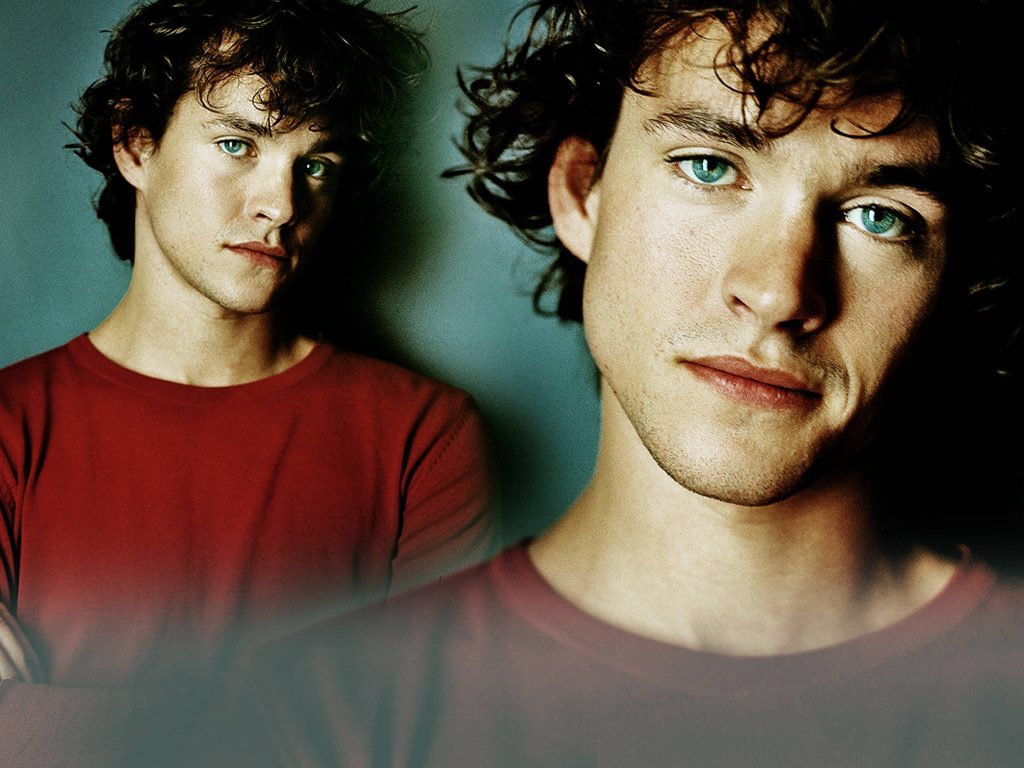 Hugh Dancy in red shirt with curly hair intense blue eyes moody background studio portrait wallpaper