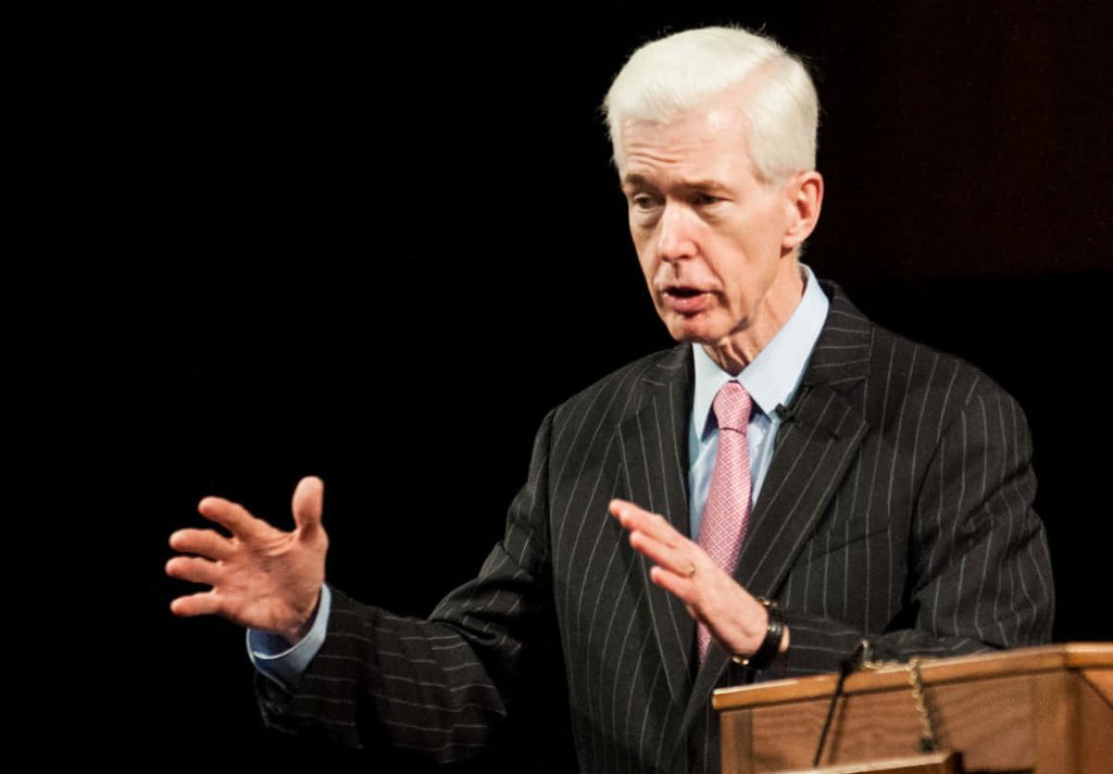 Hugh Hewitt speaking at podium in pinstripe suit and pink tie against dark background wallpaper