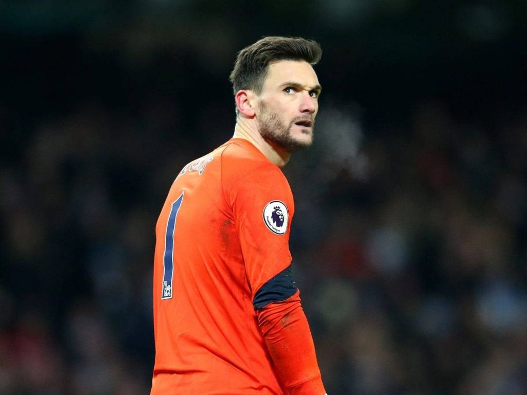 Goalkeeper Hugo Lloris in vibrant orange kit looking over shoulder with stadium background wallpaper