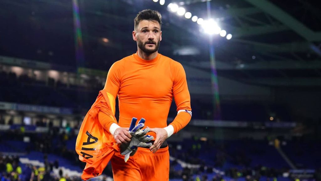 Hugo Lloris in bright orange Tottenham goalkeeper kit walking under stadium lights wallpaper