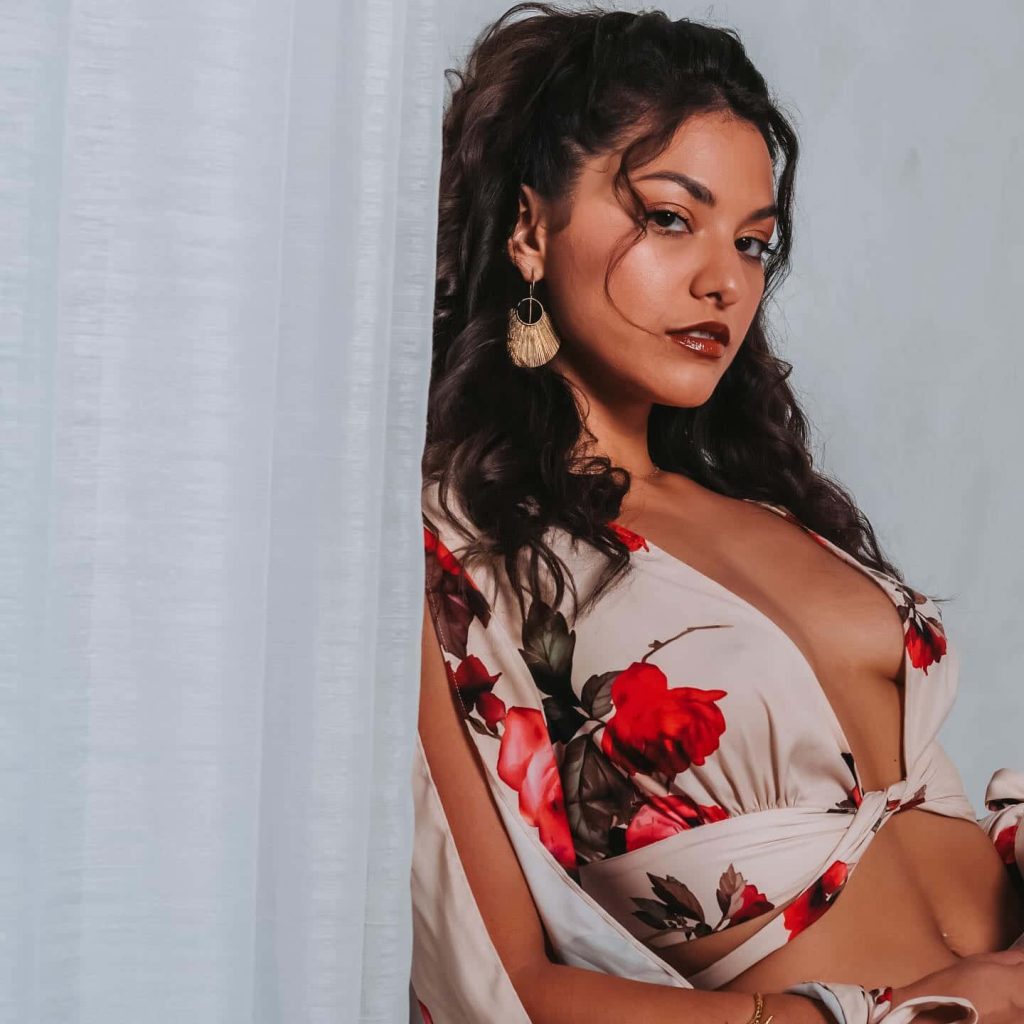 Humberly González elegant portrait in cream floral top with red roses gold earrings soft light Wallpaper