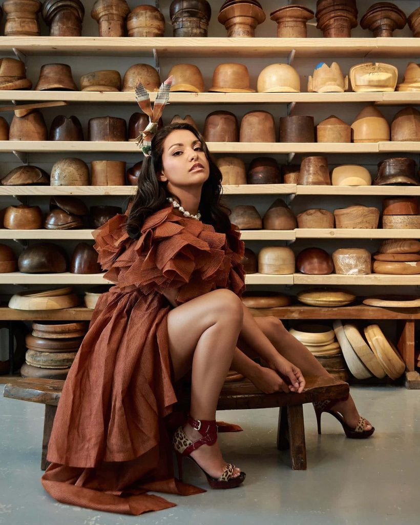 Humberly González in ruffled brown dress and animal print heels on rustic bench studio backdrop Wallpaper