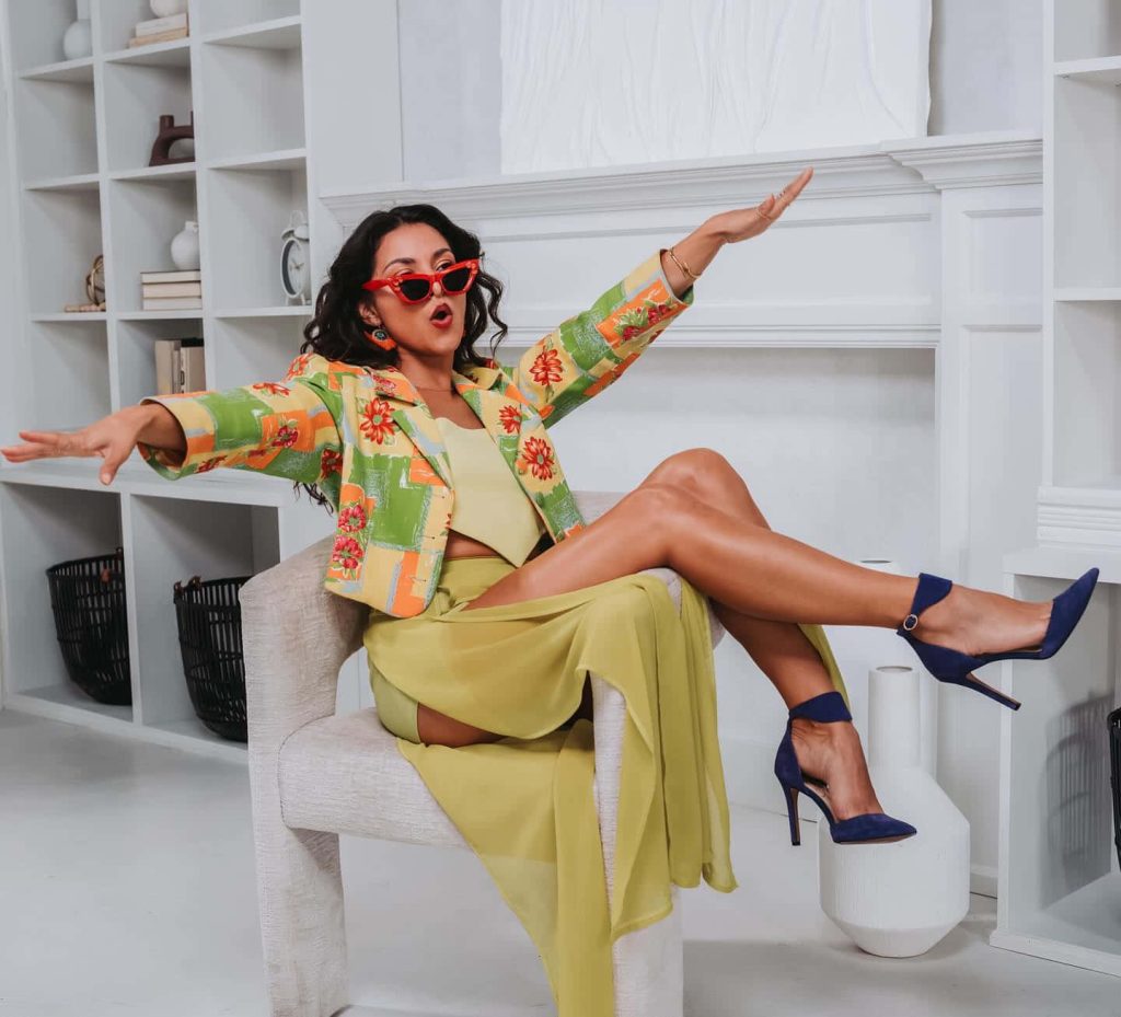 Actress Humberly González in colorful floral blazer and yellow skirt sitting in white room Wallpaper