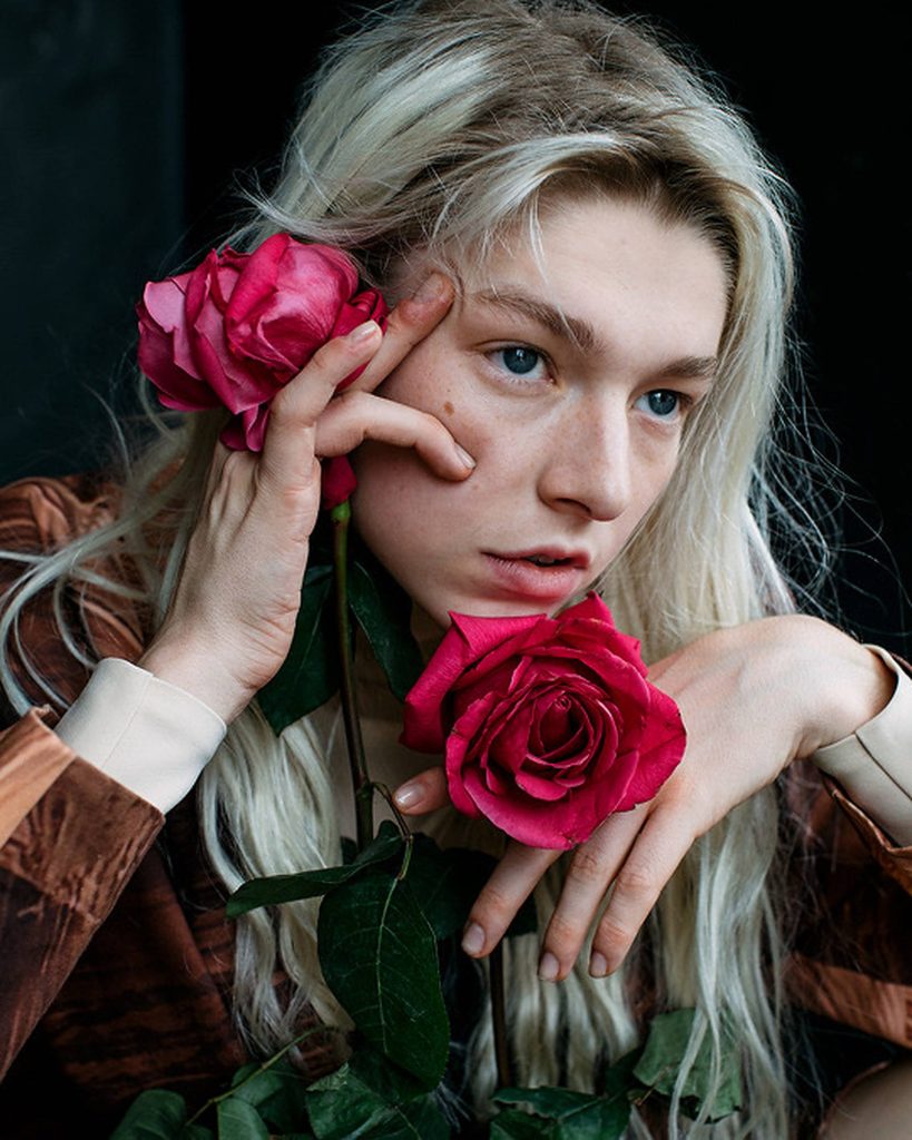Hunter Schafer with platinum blonde hair holding vibrant red roses dark minimalist background Wallpaper