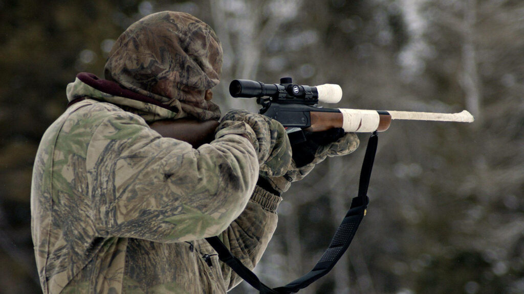 Stealthy Hunter Taking Aim: Captivating Shot of Camouflaged Man with Hunting Shotgun amidst Serene Woodland Wallpaper