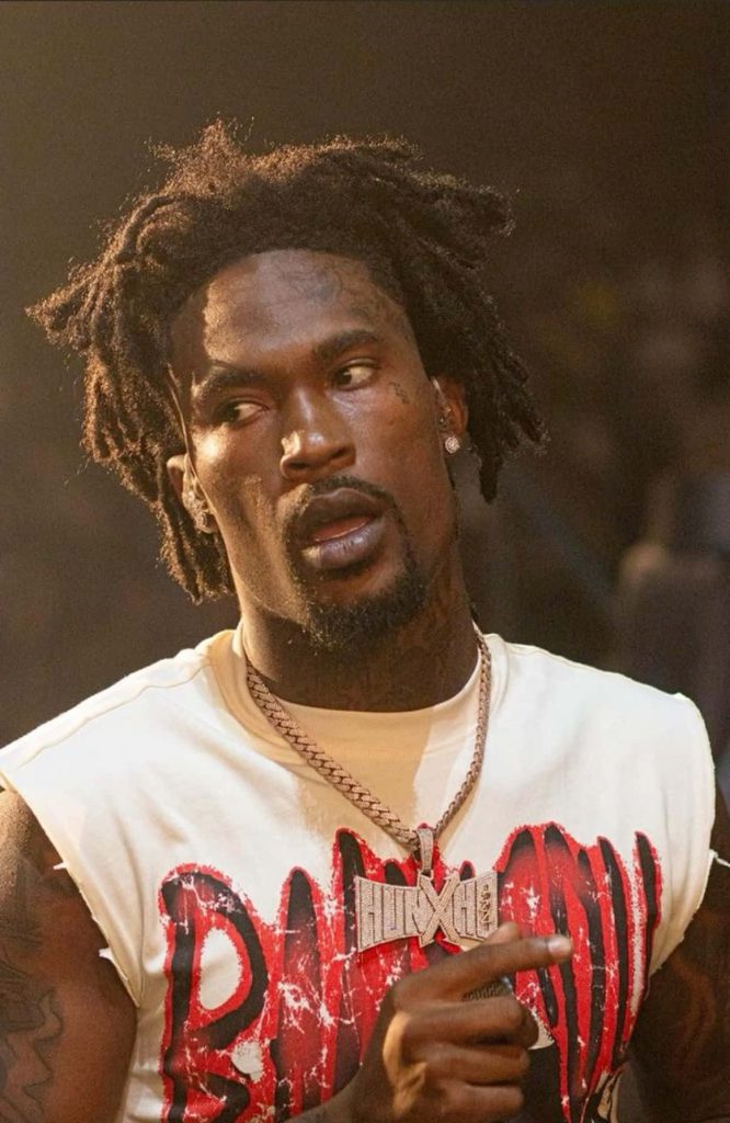Portrait of American rapper Hunxho with diamond chain dreadlocks intense gaze in stage lighting Wallpaper