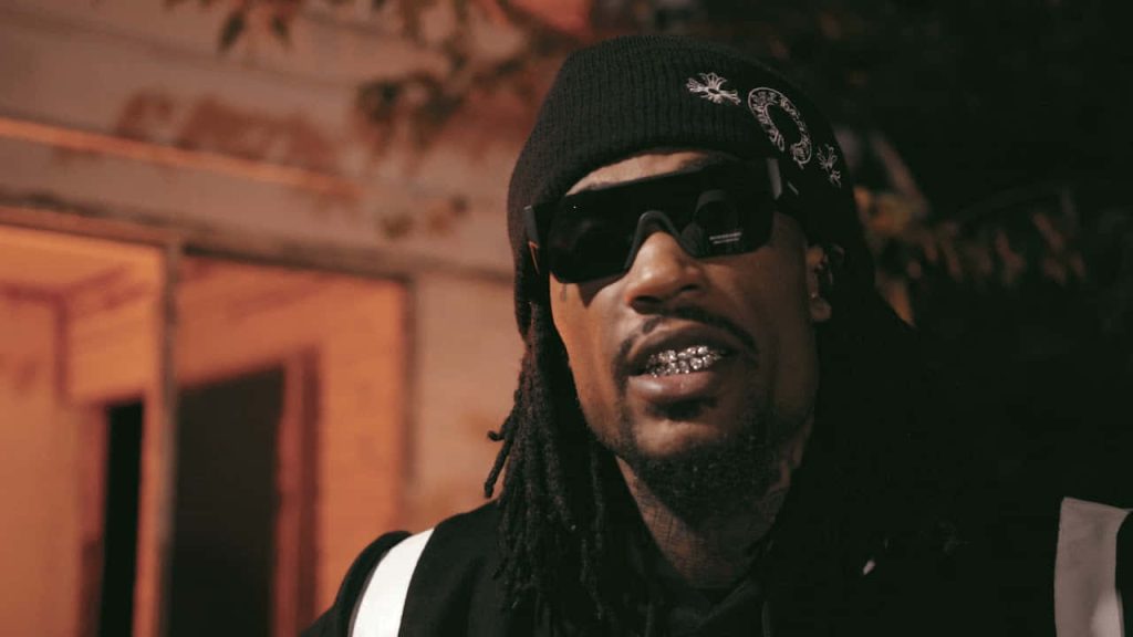 Rapper Hunxho in black beanie dark sunglasses diamond grillz gritty dimly lit urban hip-hop wallpaper